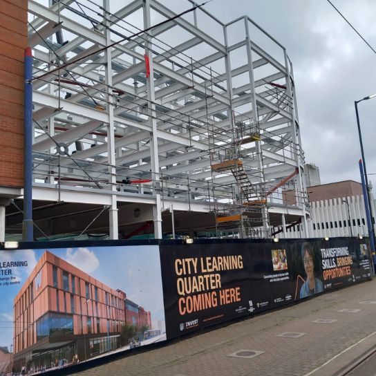 Steel framework of the new City Learning Quarter campus where the time capsule will be buried. Site surrounded by hoardings showing what the finished building will look like